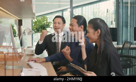 Felice tre persone del gruppo di affari eccitato, il lavoro di squadra asiatico guardando schermo del calcolatore con le mani sollevate celebra la vittoria il proje riuscito Foto Stock