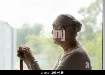 Frustrata triste solitario anziana donna seduta da vetro finestra Foto Stock