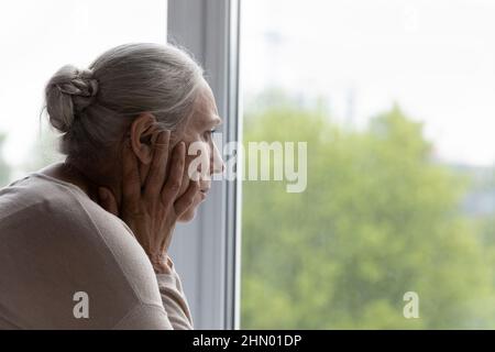 Signora anziana arrabbiato che guarda fuori dalla finestra con disperazione Foto Stock
