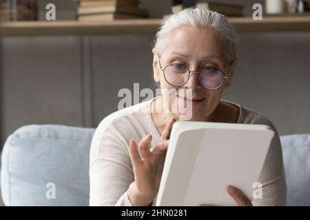 Donna utente tablet digitale senior positiva in occhiali lettura ebook Foto Stock