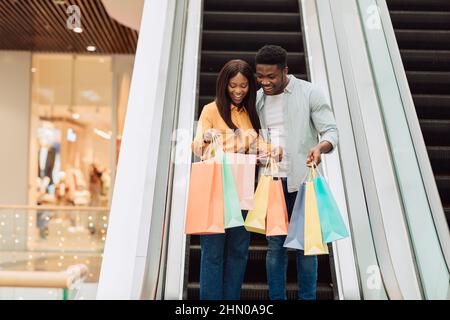 Felice coppia nera che tiene le borse della spesa guardando all'interno Foto Stock