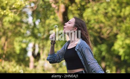 La studentessa soffia un dente d'leone in una giornata estiva. Foto Stock
