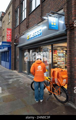 Una persona di consegna di Just Eat si prepara ad entrare in Greggs per ritirare un ordine per la consegna. Preso presto la Domenica mattina a Lower Marsh, Waterloo Londra Foto Stock