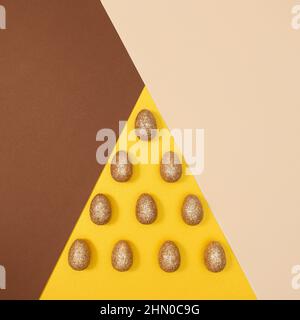 Scena pasquale con uova dorate glitterate su sfondo giallo beige pastello e brilla. Concetto minimo di posa piatta Foto Stock