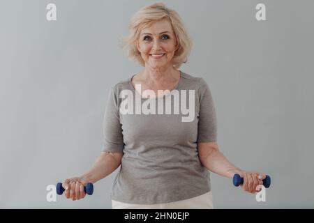 Anziano caucasico vecchia donna anziana ritratto grigio capelli facendo esercizi con manubri Foto Stock