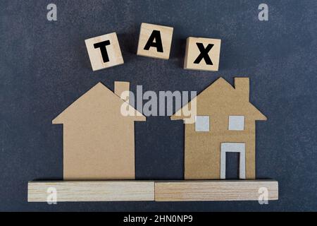 Vista di modello di casa di carta vicino blocchi di legno con testo di imposta su sfondo di legno. Concetto di imposta immobiliare. Foto Stock