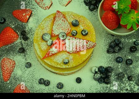 Sana colazione estiva, pancake classici americani fatti in casa con frutti di bosco freschi e zucchero a velo. Mirtilli e fragole su pancake. Nero Foto Stock