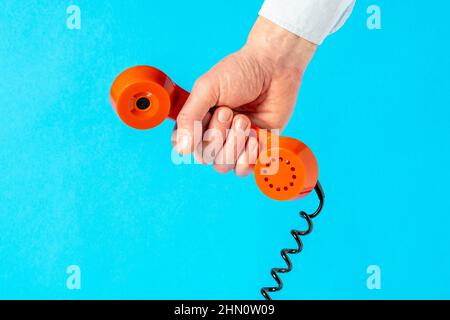 Mano che tiene vecchio ricevitore del telefono sopra blu background.Communication concetto. Foto Stock