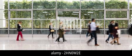 Molti anonimo la gente di affari sono a piedi attraverso un luminoso corridoio in ufficio moderno Foto Stock