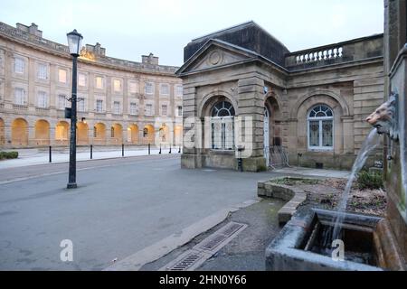 L'acqua potabile di sorgente di Buxton emana dalla fontana della testa del leone presso il pozzo di St Ann's con l'hotel Buxton Crescent e la Pump Room sullo sfondo Foto Stock