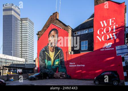 Un grande murale pubblicitario su un muro di un edificio accanto a un parcheggio nel quartiere nord di Manchester con l'iconica torre CIS. Foto Stock