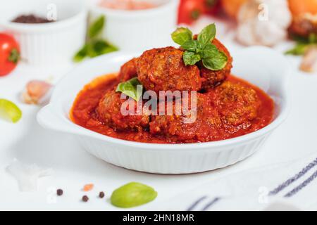 Carne sminuzzata cruda pronta per la preparazione di polpette. Decorato con ingredienti come cipolle, basilico, salsa di pomodoro, pepe e sale intorno. Foto Stock