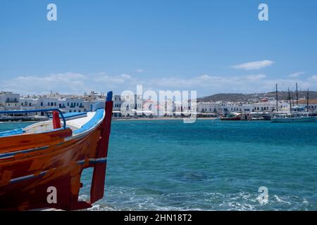 Grecia, isola di Mikonos, destinazione Cicladi. Porto di Mykonos, edificio sul lungomare imbiancato, negozio, spiaggia, sfondo blu cielo. Vista dal mare, dal mare Foto Stock