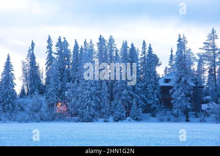 Casa nascondendosi tra alberi di abete nella neve, bella scena invernale all'aperto. Coste di Strbske pleso in alti Tatra, popolare destinazione di viaggio in Slovacchia Foto Stock