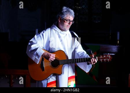 Il reverendo Bob Bailey suona la chitarra durante uno dei suoi servizi e cerimonie della chiesa alla chiesa di St Mary a Kippax, West Yorkshire UK Foto Stock