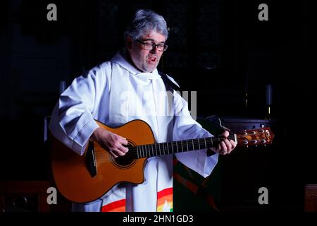 Il reverendo Bob Bailey suona la chitarra durante uno dei suoi servizi e cerimonie della chiesa alla chiesa di St Mary a Kippax, West Yorkshire UK Foto Stock