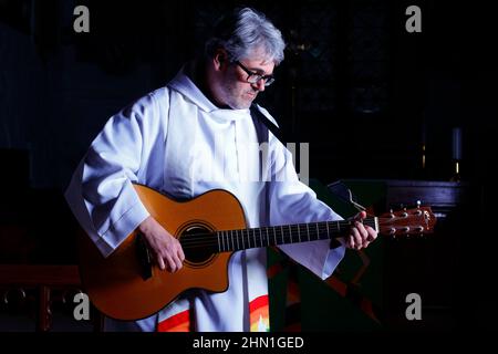 Il reverendo Bob Bailey suona la chitarra durante uno dei suoi servizi e cerimonie della chiesa alla chiesa di St Mary a Kippax, West Yorkshire UK Foto Stock