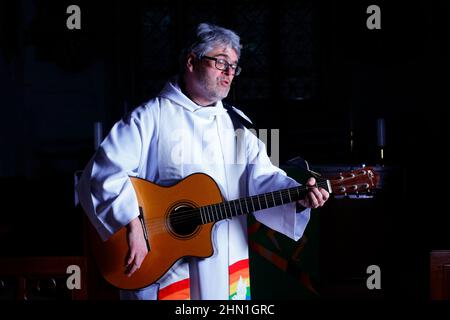 Il reverendo Bob Bailey suona la chitarra durante uno dei suoi servizi e cerimonie della chiesa alla chiesa di St Mary a Kippax, West Yorkshire UK Foto Stock