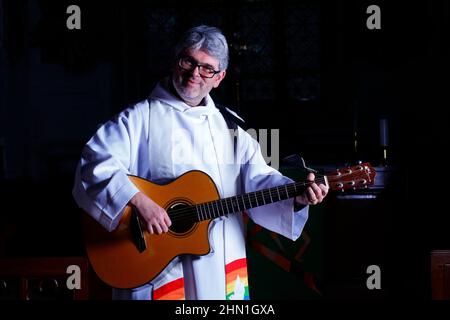 Il reverendo Bob Bailey suona la chitarra durante uno dei suoi servizi e cerimonie della chiesa alla chiesa di St Mary a Kippax, West Yorkshire UK Foto Stock