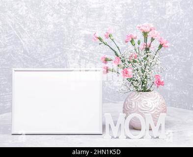 Mock up bianco telaio vuoto, vaso rosa rotondo di garofano dolce e fiori gypsophila e lettere di legno bianco MOM. Tema decorazioni del giorno della mamma. Ho Foto Stock