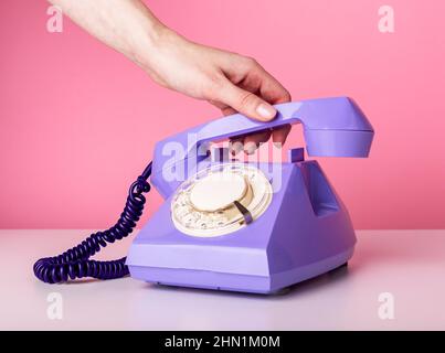 Tenere la mano retro telefono cellulare, ricevitore primo piano su sfondo rosa. Stile vintage. Foto di alta qualità Foto Stock