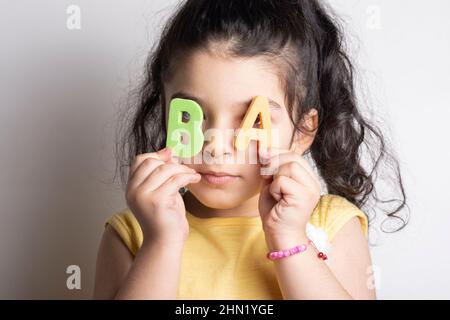 Bambina che tiene due lettere AB dell'alfabeto spugnoso davanti ai suoi occhi Foto Stock