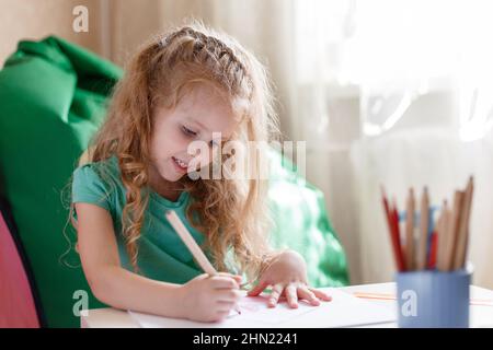 Bambina bambino bambino nella stanza dei bambini disegna con interesse da matite in stanza dei bambini. 5 anni felice sorridente ragazza prescolare attira in camera da solo Foto Stock