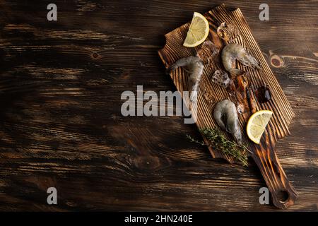 Gamberetti crudi con fette di limone e cubetti di ghiaccio sul tagliere su sfondo di legno, gamberi di mare congelati. Foto Stock