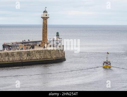 Barca gialla che lascia Whitby Harbour, oltrepassa il faro Foto Stock