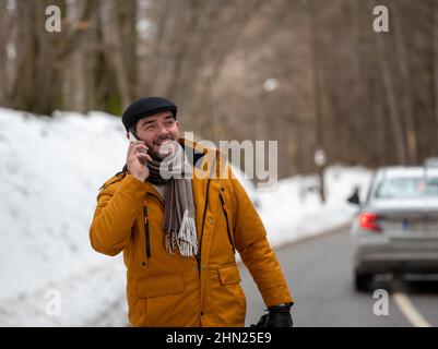 Uomo in piedi sulla strada in giacca in inverno freddo prendendo chiamata di emergenza dopo che la sua auto si è rotta Foto Stock