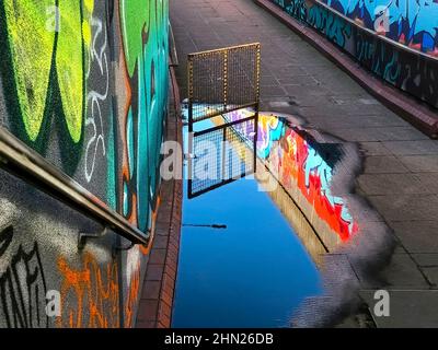 Scendete fino al sottopassaggio sotto una strada principale di Leicester che riflette le pareti coperte di graffiti nella pozza della pioggia Foto Stock