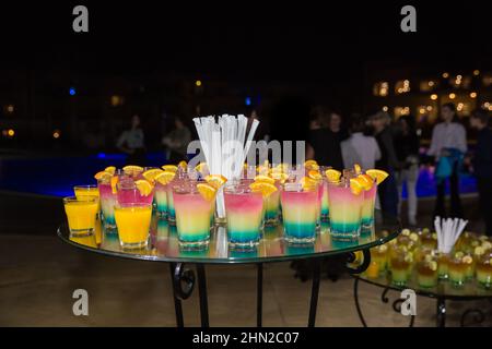 Cocktail alcolici di diversi colori con fette d'arancia in un party notturno all'aperto in Egitto hotel. Tavolo in vetro decorato per catering all'aperto Foto Stock