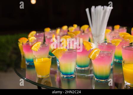 Cocktail alcolici di diversi colori con fette d'arancia in un party notturno all'aperto in Egitto hotel. Tavolo in vetro decorato per catering all'aperto Foto Stock