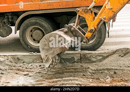 Lavori stradali sulla strada della città. La benna dell'escavatore raccoglie la vecchia pavimentazione e la carica in un dumper. Foto Stock