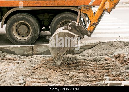 Lavori stradali sulla strada della città. La benna dell'escavatore raccoglie la vecchia pavimentazione e la carica in un dumper. Foto Stock