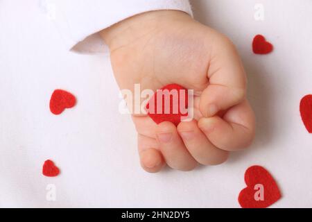 Una mano del bambino che tiene i cuori rossi sentiti. Foto Stock