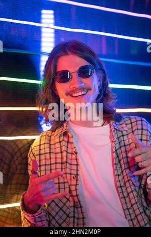 Ritratto di un giovane millenario in stile neon moderno e simbolo rock, gesto della mano. Foto Stock