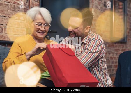 nonna che riceve un regalo in un sacchetto rosso per il giorno della nonna dal suo nonno adulto uomo. Foto di alta qualità Foto Stock