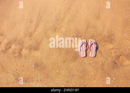 Un paio di infradito rosa per bambini su sabbia liscia fornisce spazio copia a sinistra per qualsiasi vacanza e inferenza vacanza. Foto Stock