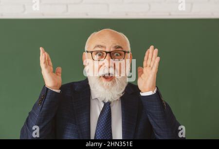 Vecchio volto sorpreso di divertente insegnante. Professore senior eccitato in lavagna. Foto Stock