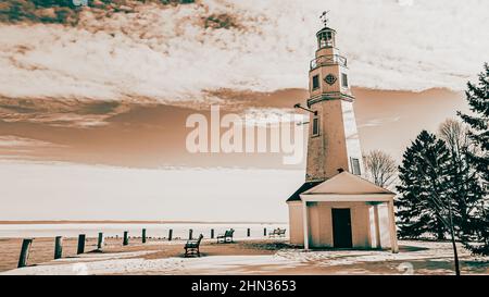 Terra coperta di neve e lago coperto di ghiaccio questo vecchio faro fa parte dei parchi pubblici e si erge a guardare le acque Foto Stock