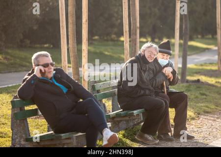 Foto di bianchi uomini caucasici seduti e discutere su una panchina a belgrado, Serbia indossare una maschera protettiva sotto il naso durante la Th Foto Stock