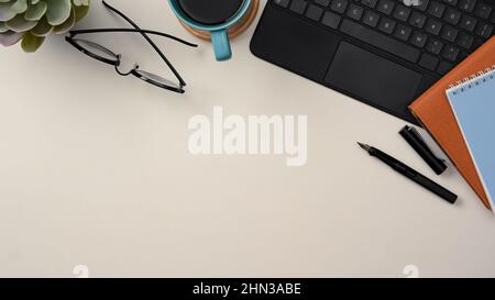 Moderno tavolo da studio con occhiali, pianta in una pentola, tazza da caffè, notebook, penna, tastiera tablet e spazio di copia su sfondo bianco. Vista dall'alto Foto Stock