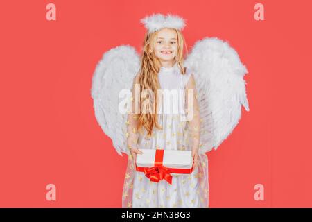Angelo dei bambini con regalo. Piccolo angelo con ali bianche contiene il regalo. Ragazza angelica giocosa. Ragazza carina dell'angelo con le ali degli angeli Foto Stock