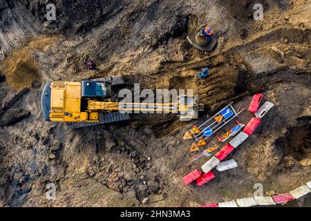 Vista dall'alto aerea sul terreno di scavo dell'escavatore cingolato per la revisione della strada. Le macchine da costruzione eseguono lavori pesanti ad alta intensità di energia su progetto. Foto Stock