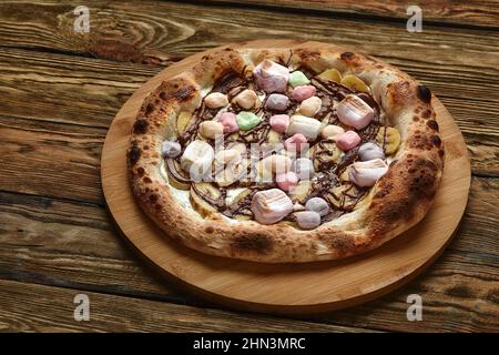 Pizza dolce intera servita con marshmallows e caramelle su sfondo di legno Foto Stock