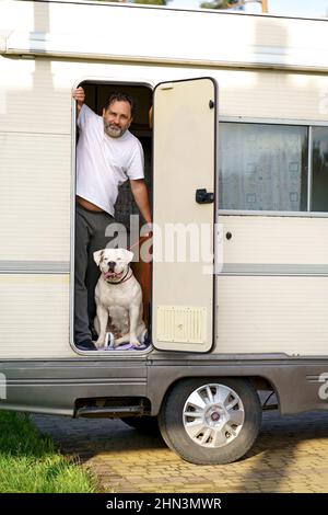 il concetto di viaggiare con un animale domestico. Un uomo con un cane bruldog americano carino razza viaggia in un motorhome. Foto Stock