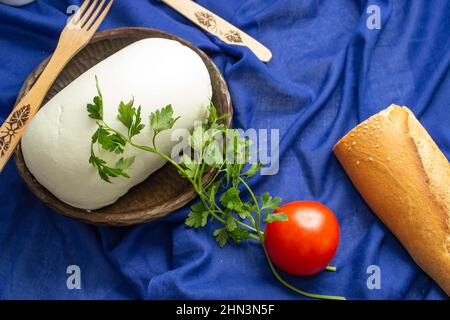 Formaggio contadino su una ciotola di legno con pane su sfondo tessile blu Foto Stock