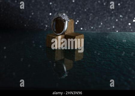 Anello in argento diamante su piccoli cubetti di legno, isolato su sfondo nero, con riflessi di vetro Foto Stock