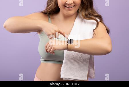 Sorridente giovane europea più taglia donna in sportswear controlla impulso sul fitness tracker Foto Stock